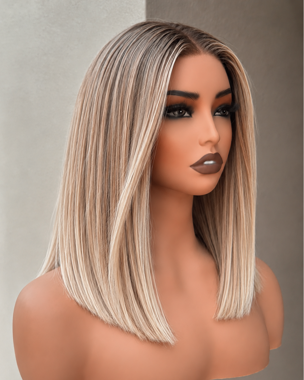 A shoulder-length straight wig with side-swept bangs on a mannequin bust, featuring a highlighted blend of light brown and blonde tones against a neutral gray background.